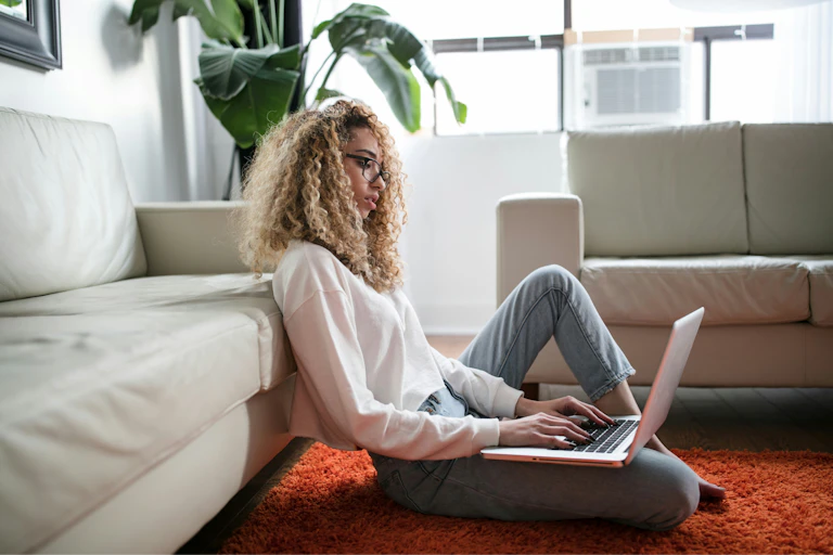 A woman sitting on the floor using her laptop.