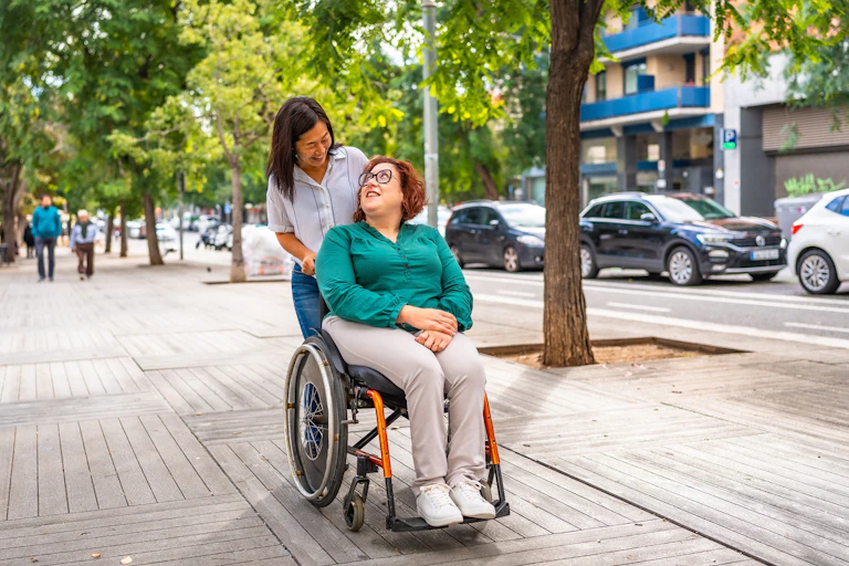 Une femme en pousse une autre, assise dans un fauteuil roulant.