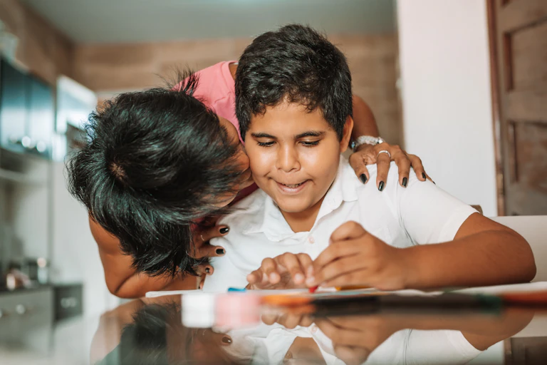 Uma mãe abraça seu filho, que está fazendo o dever de casa.