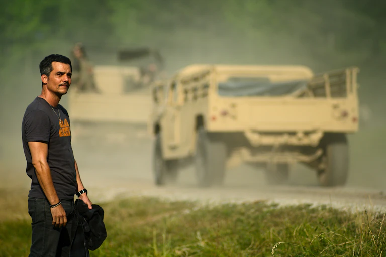Un hombre mira una carretera por la que pasan camiones militares.