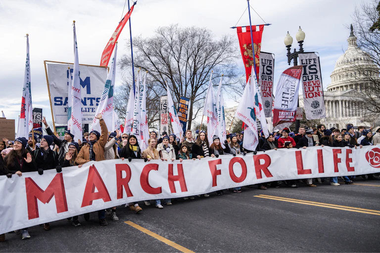 A group of protesters walk down a street holding a large "March for Life" banner.