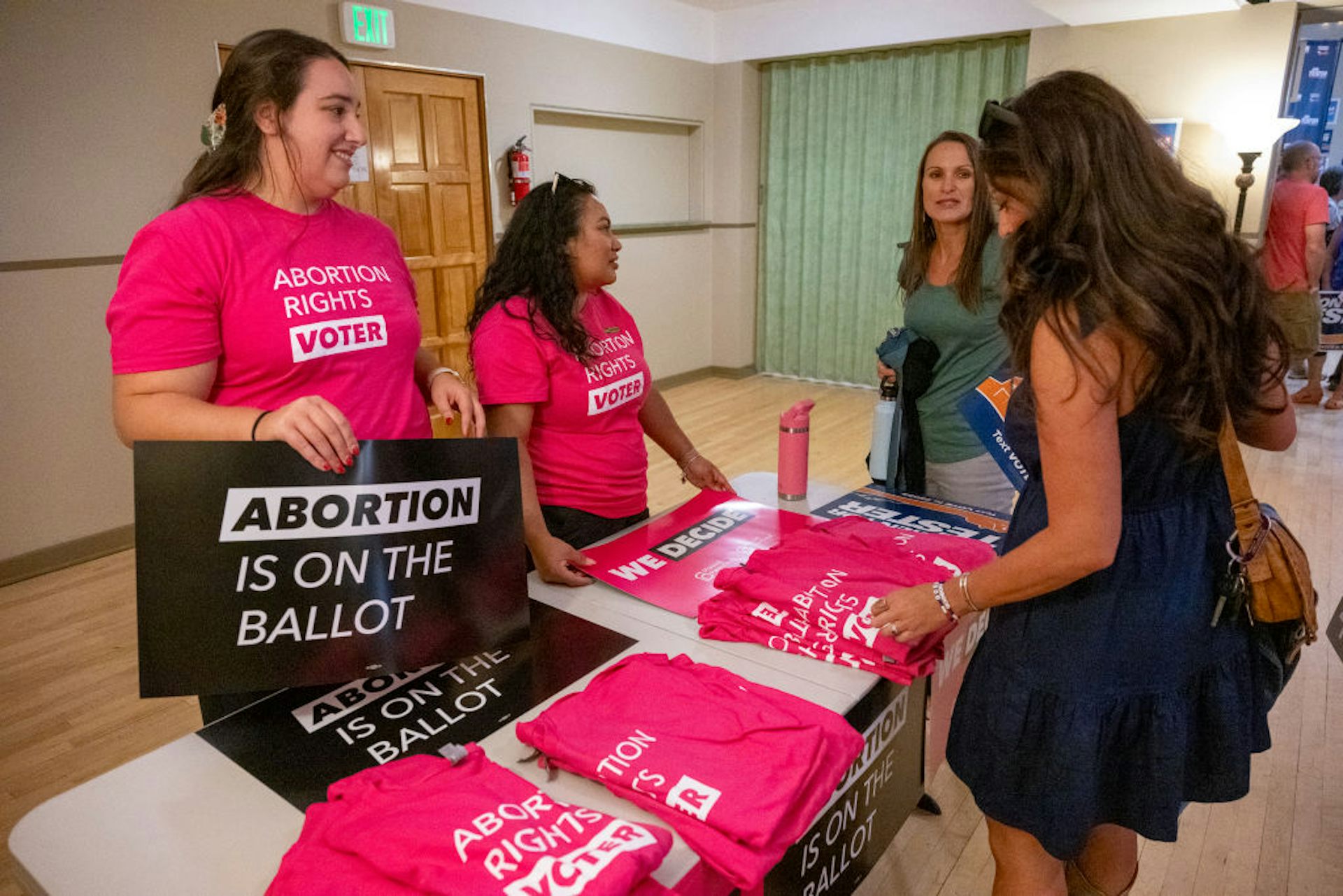 A group of women stand around a table and prepare signs and t-shirts that include messages supporting abortion rights.