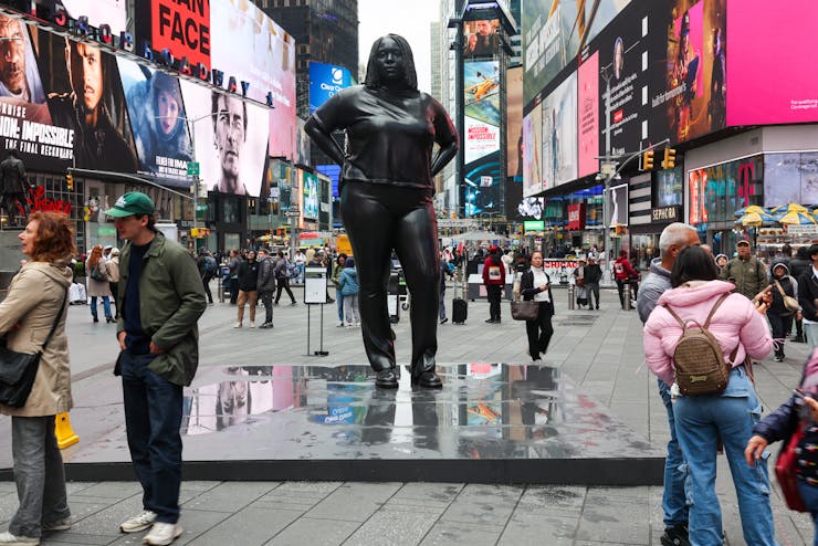 black statue of a clothed modern woman, in a busy city plaza