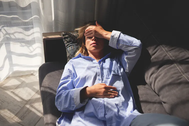 Person lying on couch, hands over forehead, eyes and stomach