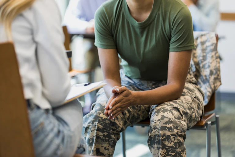 A woman in military uniform sits opposite another woman holding a clipboard