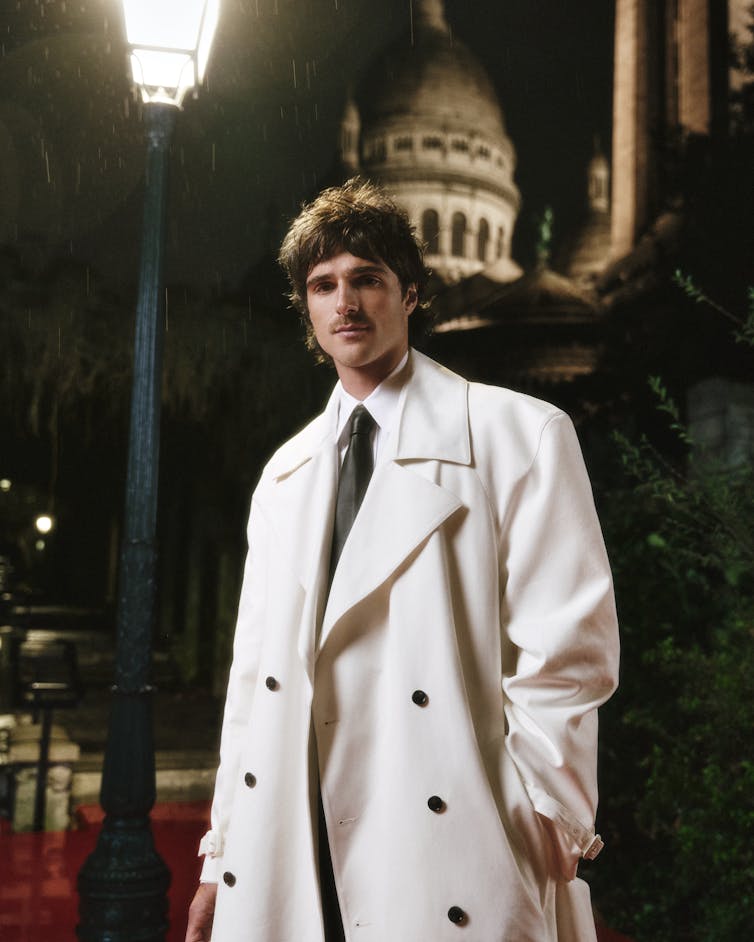 Jacob Elordi wears a white coat while posing on the red carpet in Paris.