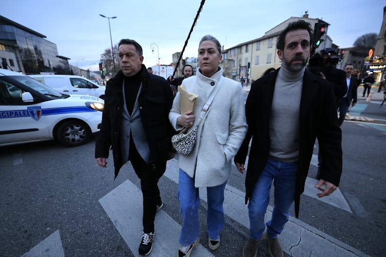 two young men and a woman cross a road grimly