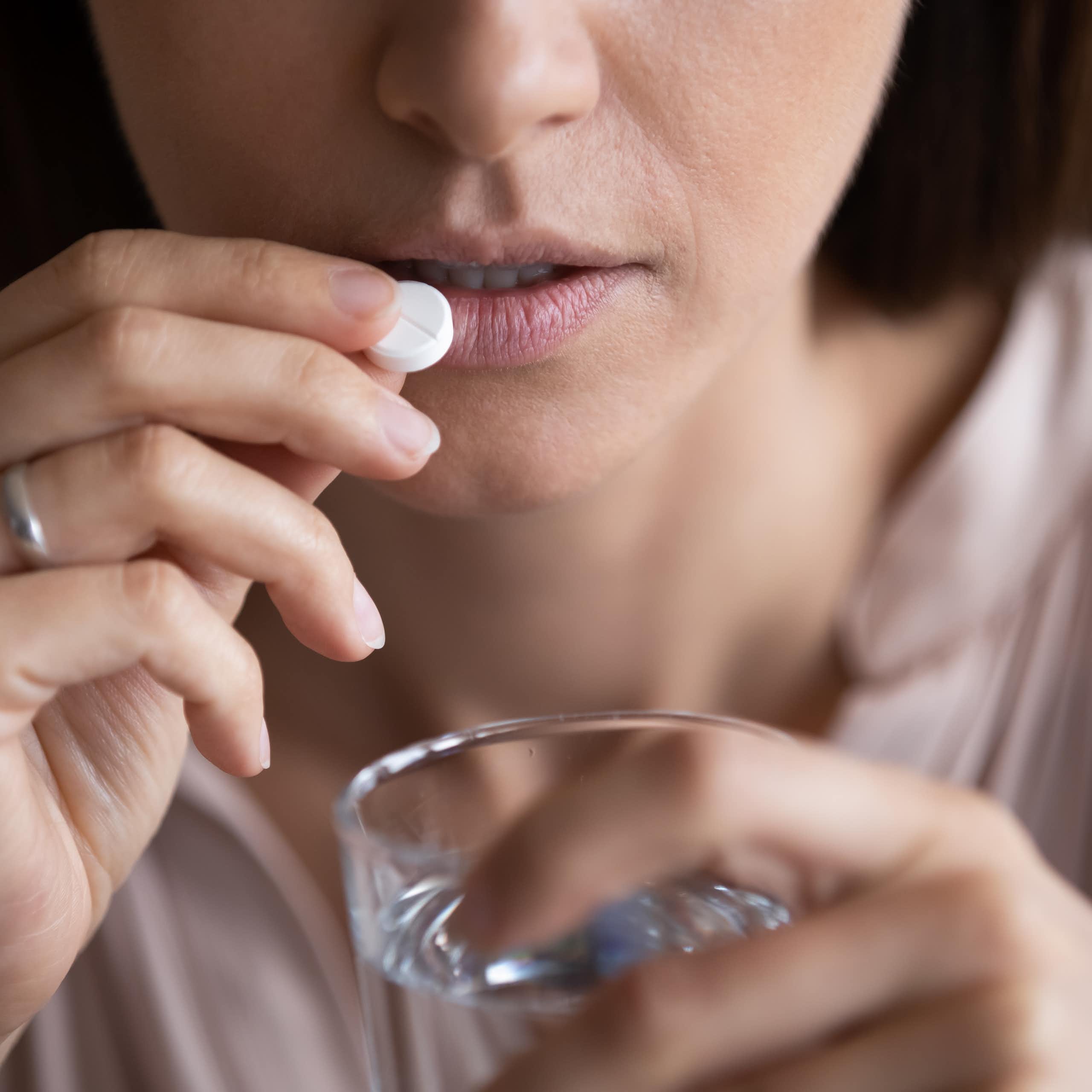 Una dona pren una pastilla amb un got d'aigua a les mans