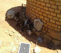 A mudbrick house and a very small, A4 size solar panel outside in the sun charging