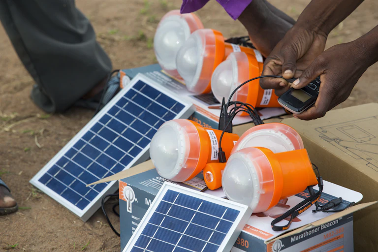 Blue rectangular panels and orange plastic lanterns; hands holding a cellphone connected to a device with wires