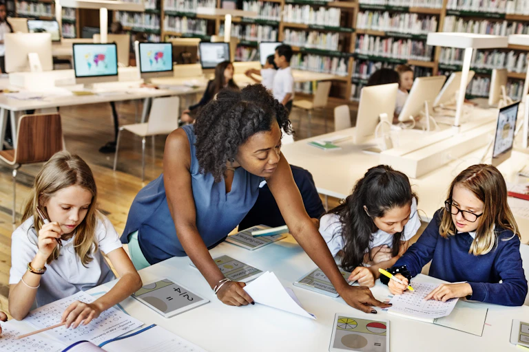 Teacher helping pupils with tablets in library