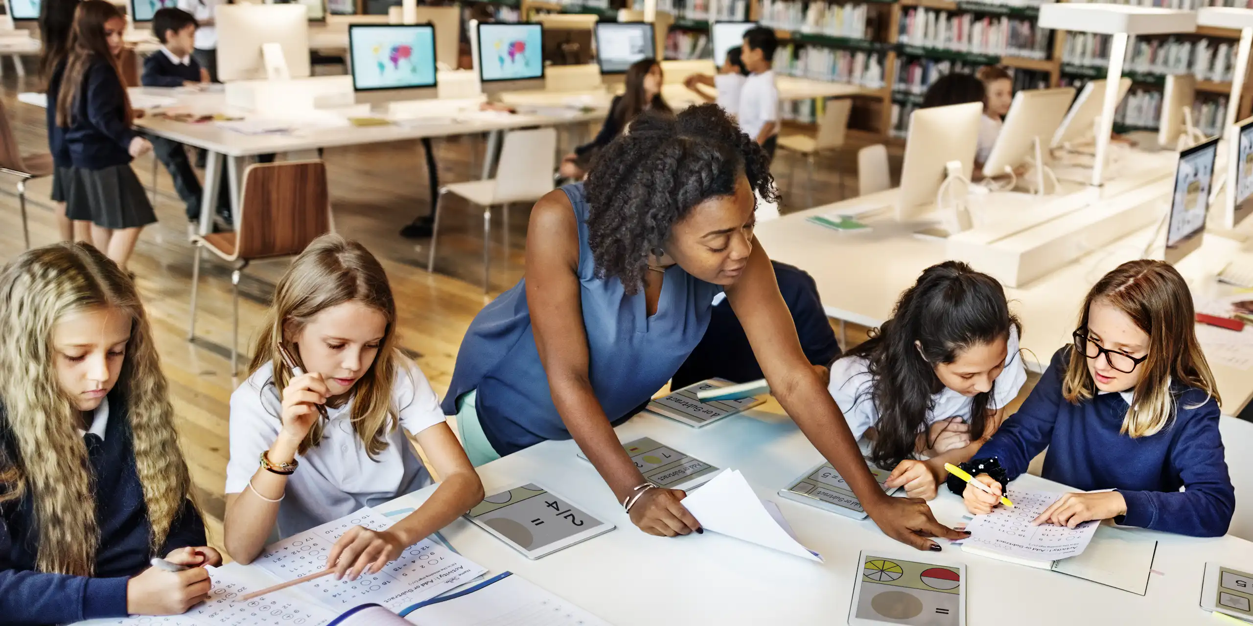 Teacher helping pupils with tablets in library