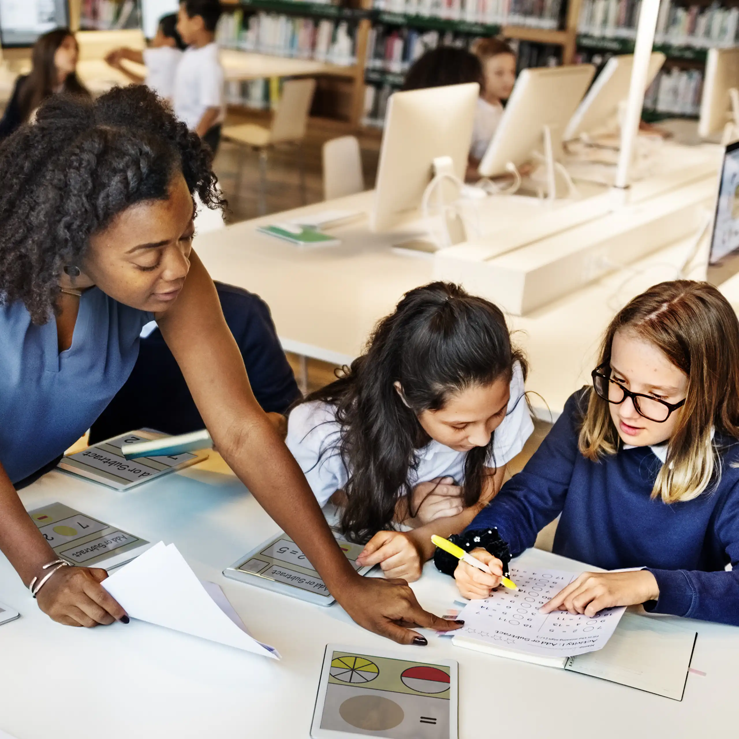 Teacher helping pupils with tablets in library
