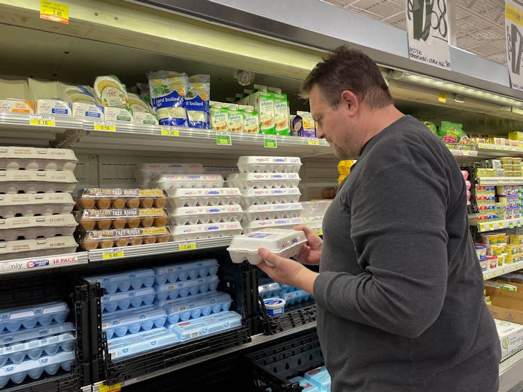a white male shopper looks at a box of eggs in the supermarket.