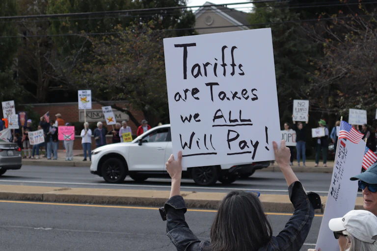 female protester holds up a sign saying tariffs are taxes we all will pay