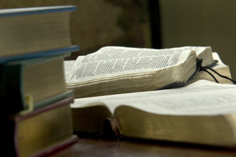 Two open books rest on a table next to a pile of three more books.