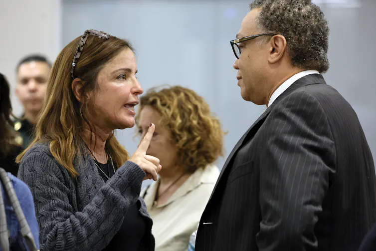 A woman wags her finger while addressing a man at close range.