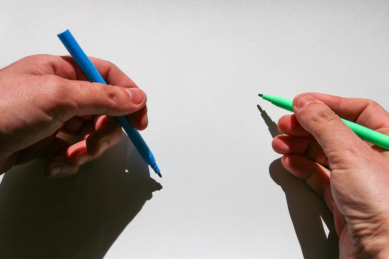 Close-up of a pair of hands holding writing utensils against a surface