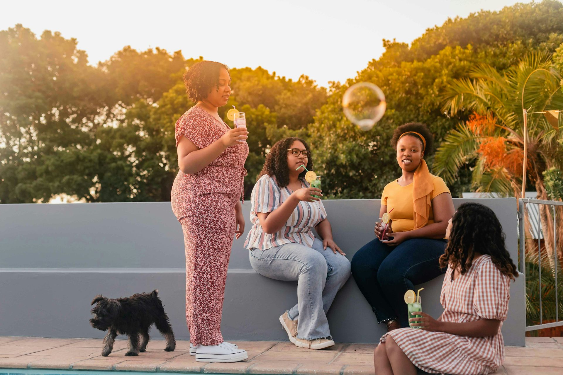 Four Black women sitting outdoors in a relaxed discussion with a large bubble floating overhead.  