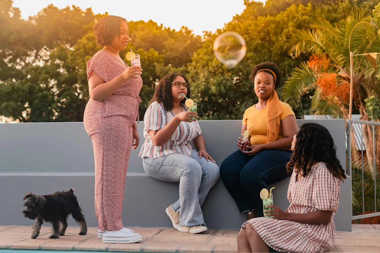 Four Black women sitting outdoors in a relaxed discussion with a large bubble floating overhead.