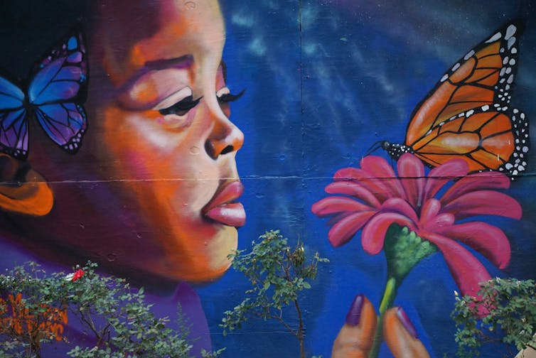 Necesitamos hablar sobre cómo las educadoras negras experimentan agotamiento y preocupación. 1 Un mural pintado de una mujer negra mirando suavemente una mariposa.