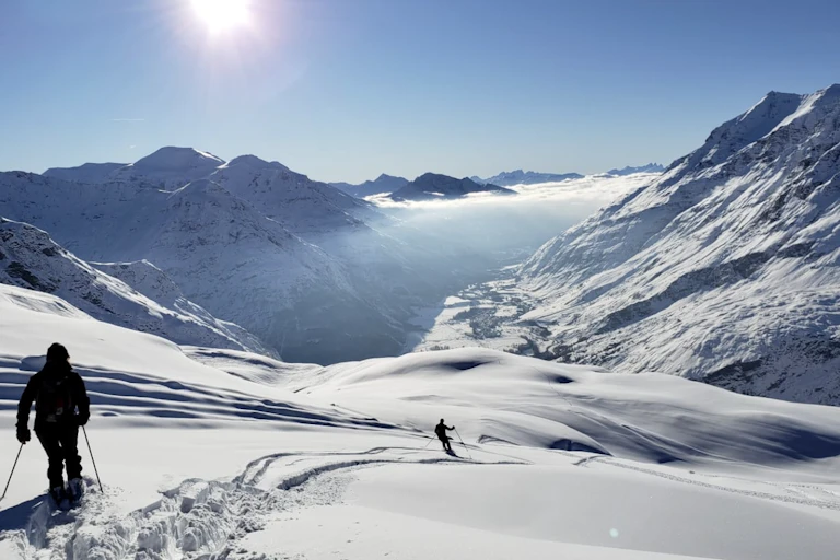 Off-piste skiers head down a slope with snow-capped mountains in the background