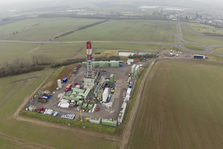 A large drilling tower sits in an open, grassy area.