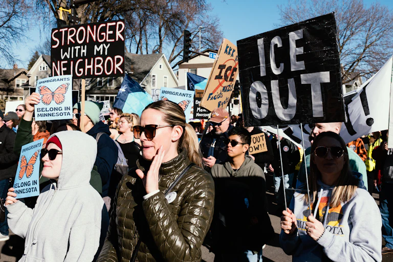 People march together, with signs saying things like 'ICE Out.'