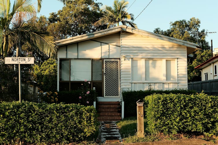 The facade of a white weatherboard house surrounded by palm trees
