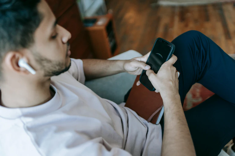 A man sitting on a couch, scrolling on his phone.