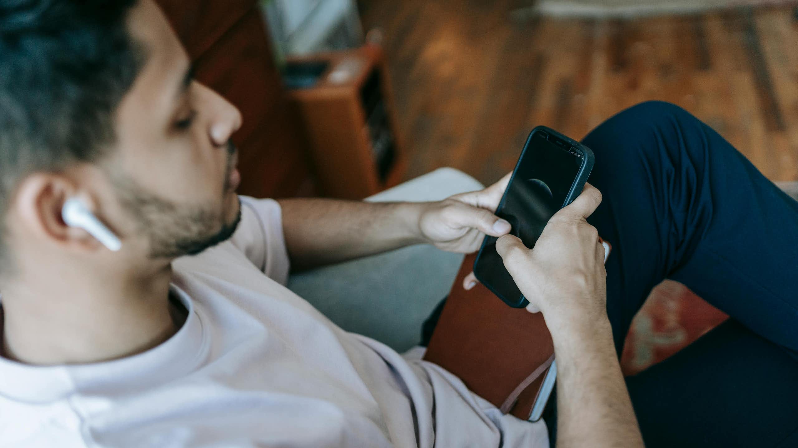A man sitting on a couch, scrolling on his phone.