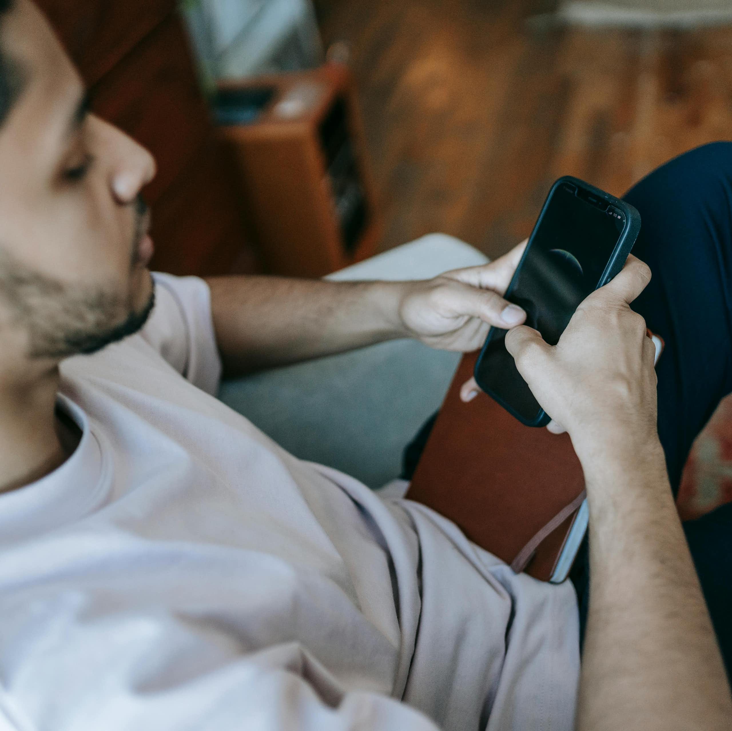 A man sitting on a couch, scrolling on his phone.