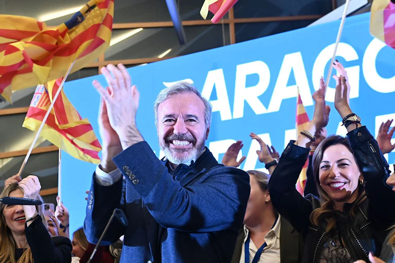 Un hombre sonriente aplaude rodedado de otras personas y banderas.