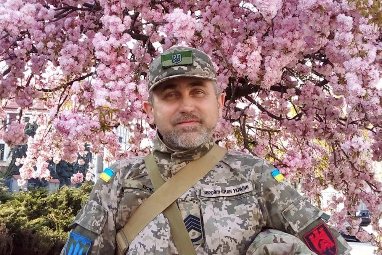 A Ukrainian soldier against a backdrop of pink blossom