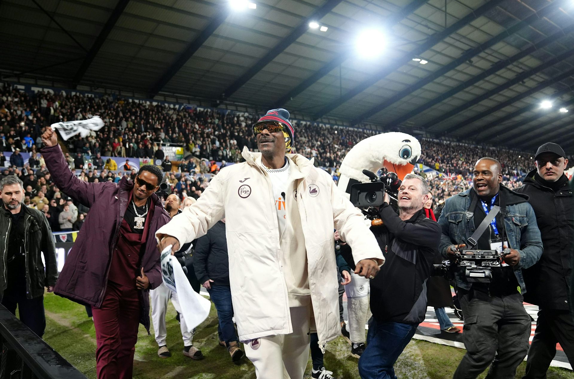 Snoop Dogg on the pitch at the Swansea.com stadium wearing club kit surrounded by camera operators. 