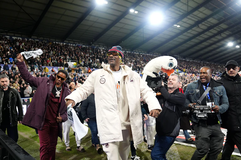 Snoop Dogg on the pitch at the Swansea.com stadium wearing club kit surrounded by camera operators.