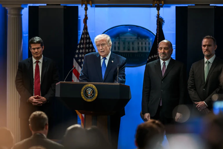 A man giving a speech behind a podium surrounded by other three men.