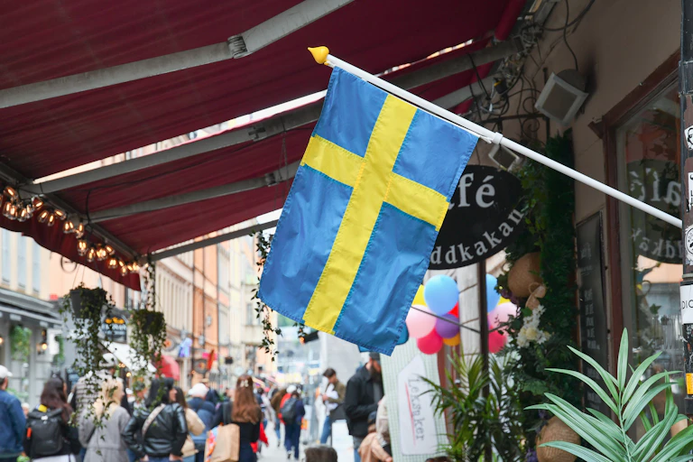a swedish flag hangs outside a cafe in stockholm with people passing by in the street
