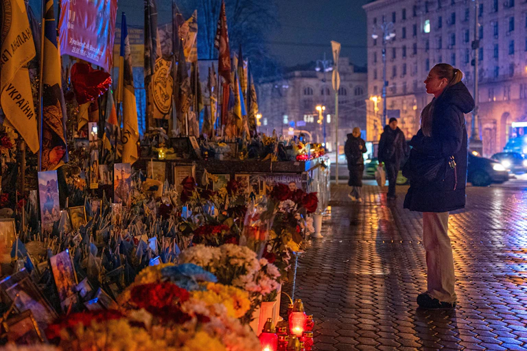 A woman stands looking at a display of flowers and Ukrainian flags.
