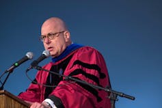 A bald man in glasses wearing a red robe.