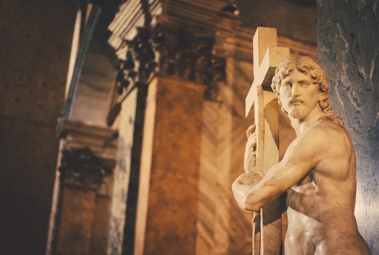 stone statue of man holding a large cross, in church setting