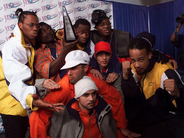 Cómo los Junos ayudaron a definir la industria musical canadiense 3 Un grupo de artistas se agachó y se reunió para posar para una foto, algunos en la parte de atrás sosteniendo la estatua.