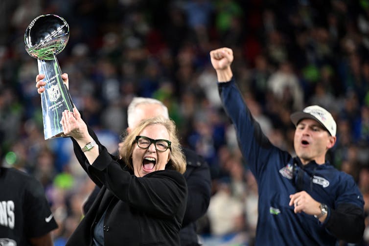 An ecstatic woman holds a shiny trophy aloft while a man behind her pumps his fist into the air.