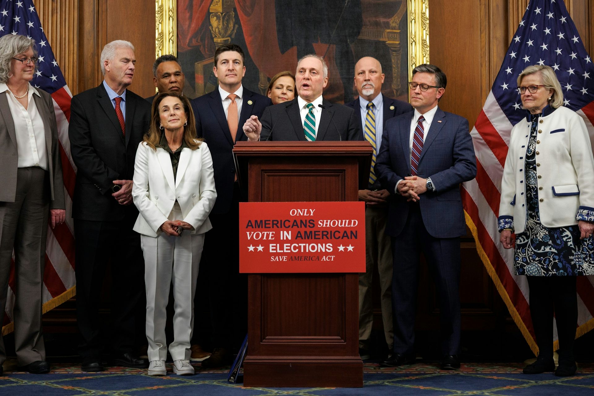 a group of men and women in formal wear stand around a podium that says ‘only americans should vote in american elections’