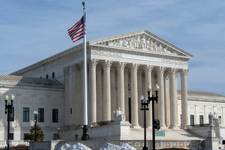 A greco-roman style white building with pillars and an American flag flying in front