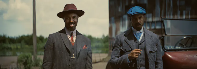 Two men stand side by side, one smiling (left) and the other holding a cigar (right).