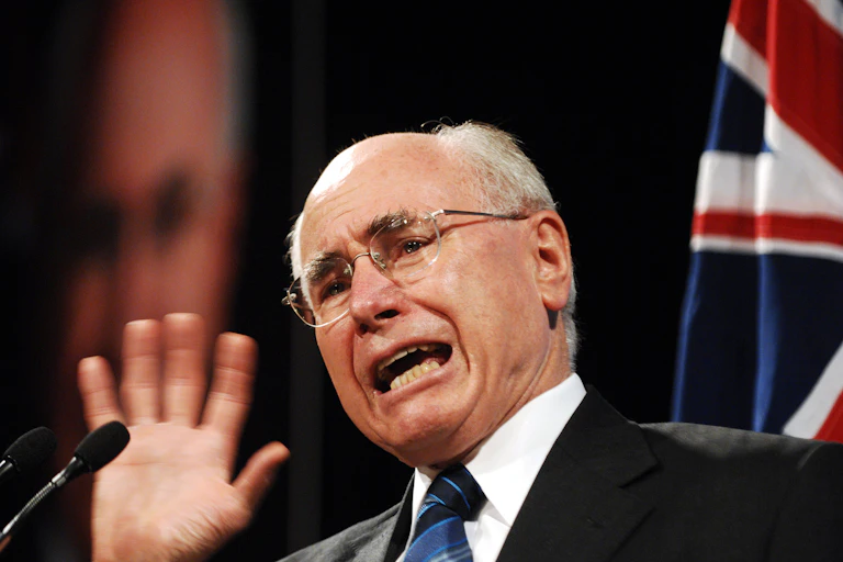 John Howard, an older balding man in a suit and tie, with an Australian flag