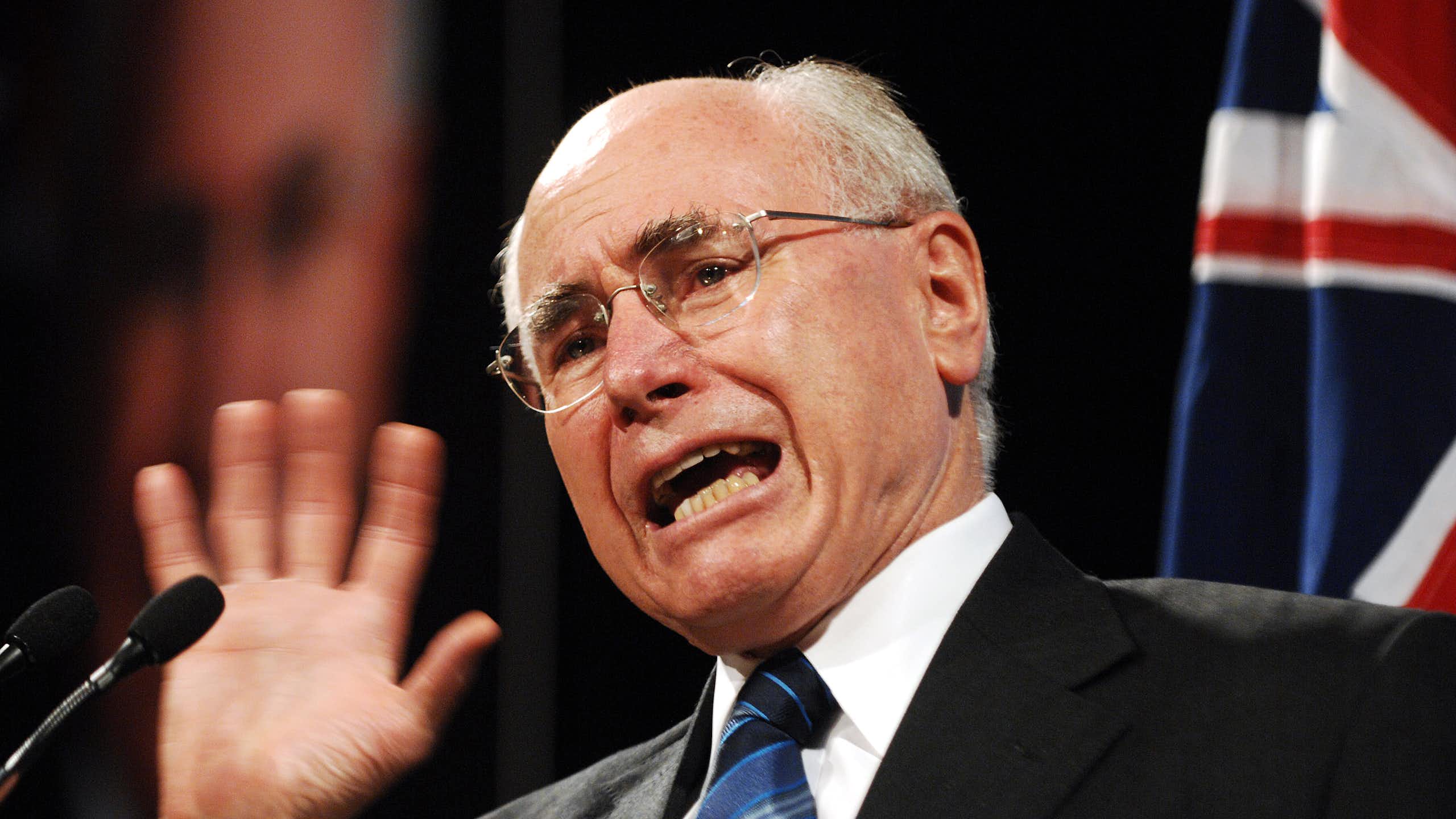 John Howard, an older balding man in a suit and tie, with an Australian flag