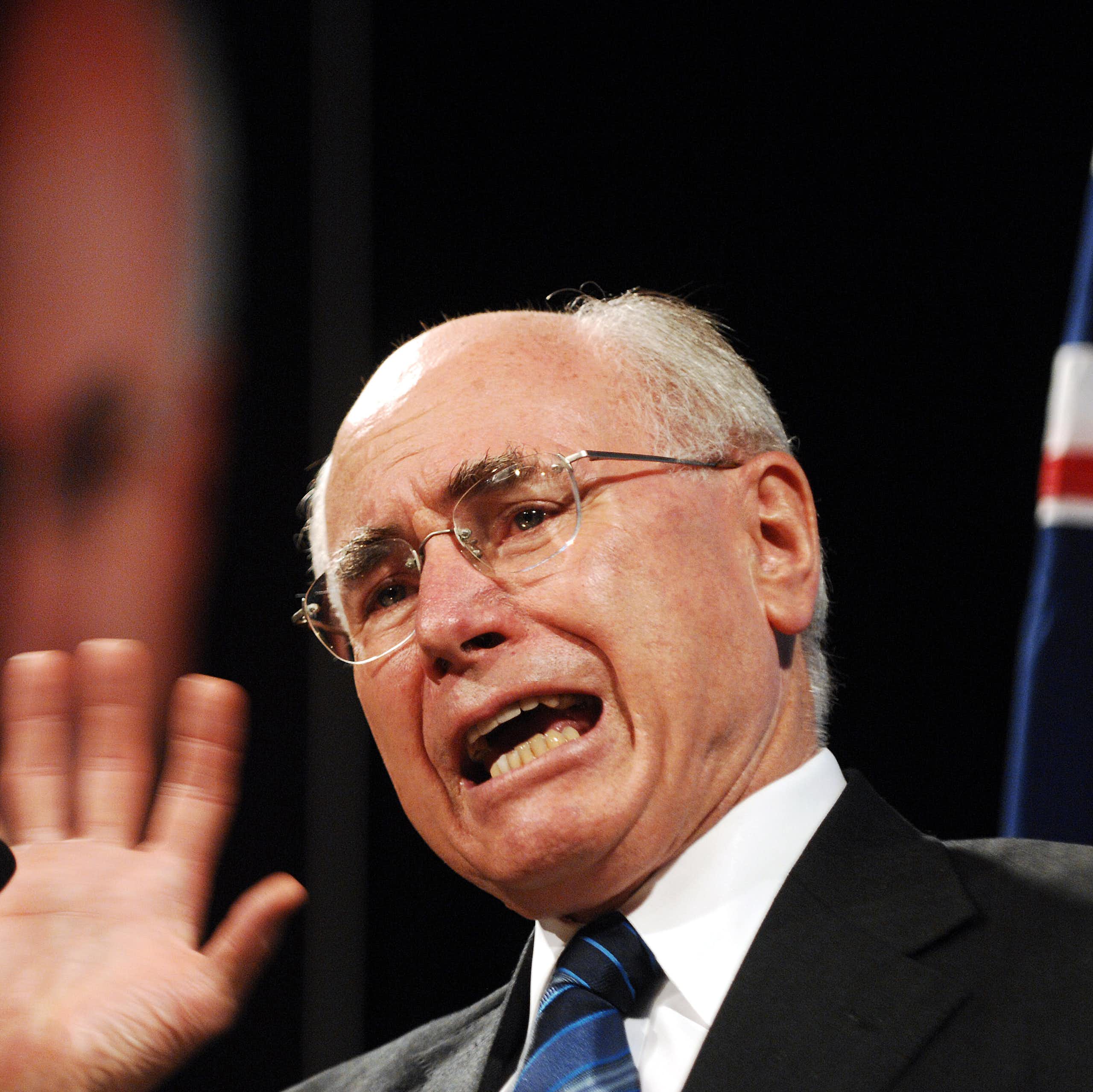 John Howard, an older balding man in a suit and tie, with an Australian flag