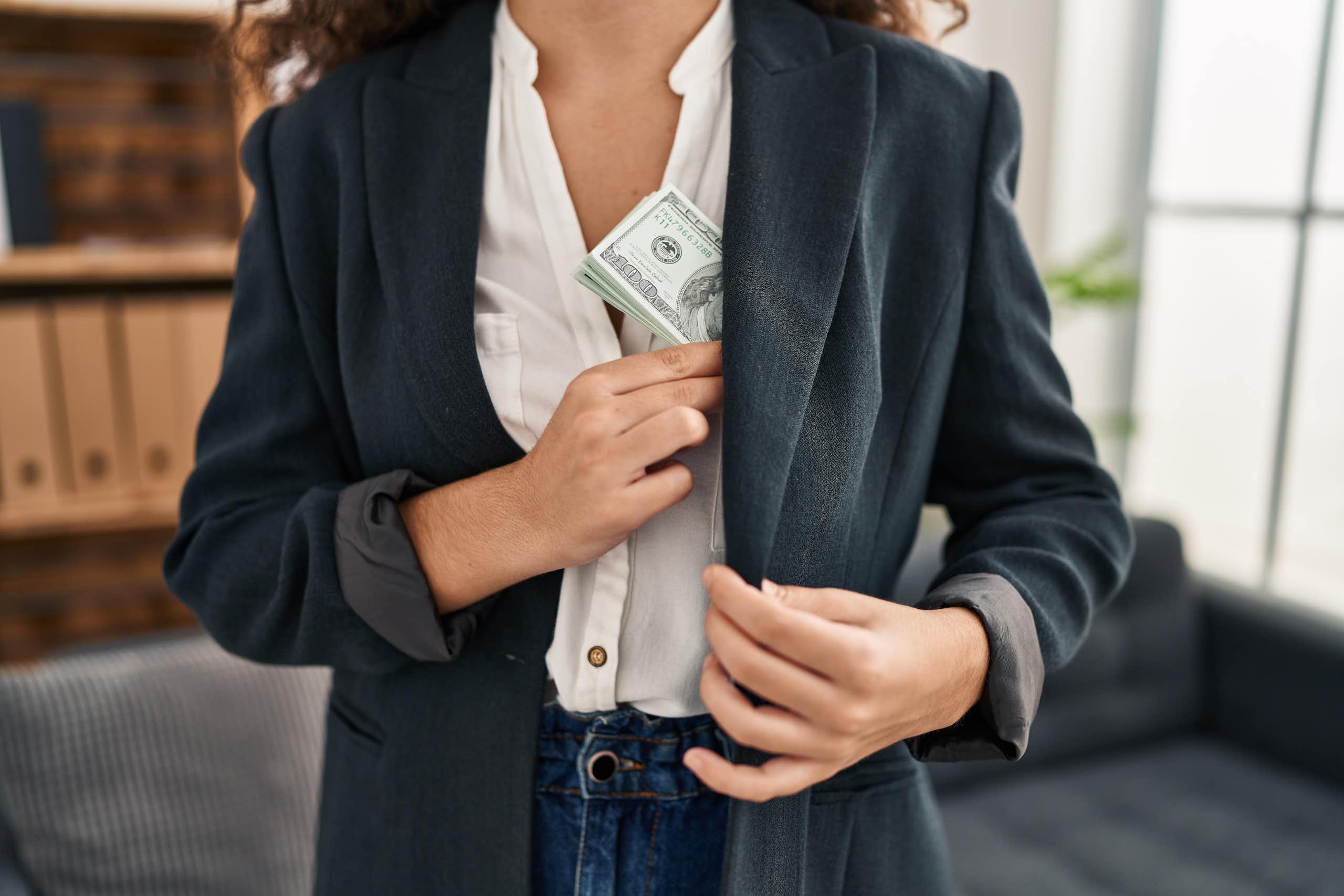 A stock image of a Latino woman putting a wad of US dollars in her pocket.